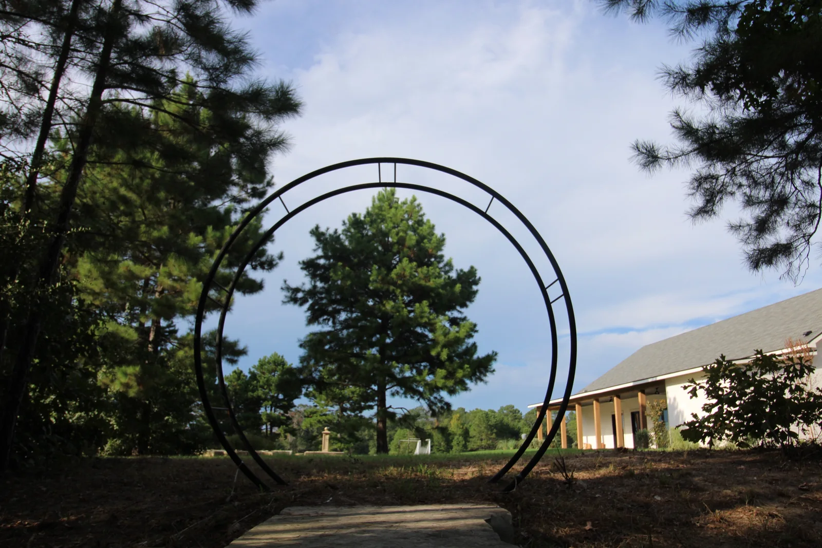 Circular metal garden arch framing a pine tree and the ranch grounds