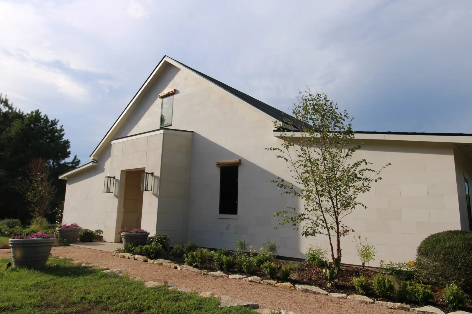 Gabled front of the pale ranch home with dark windows and landscaped garden beds