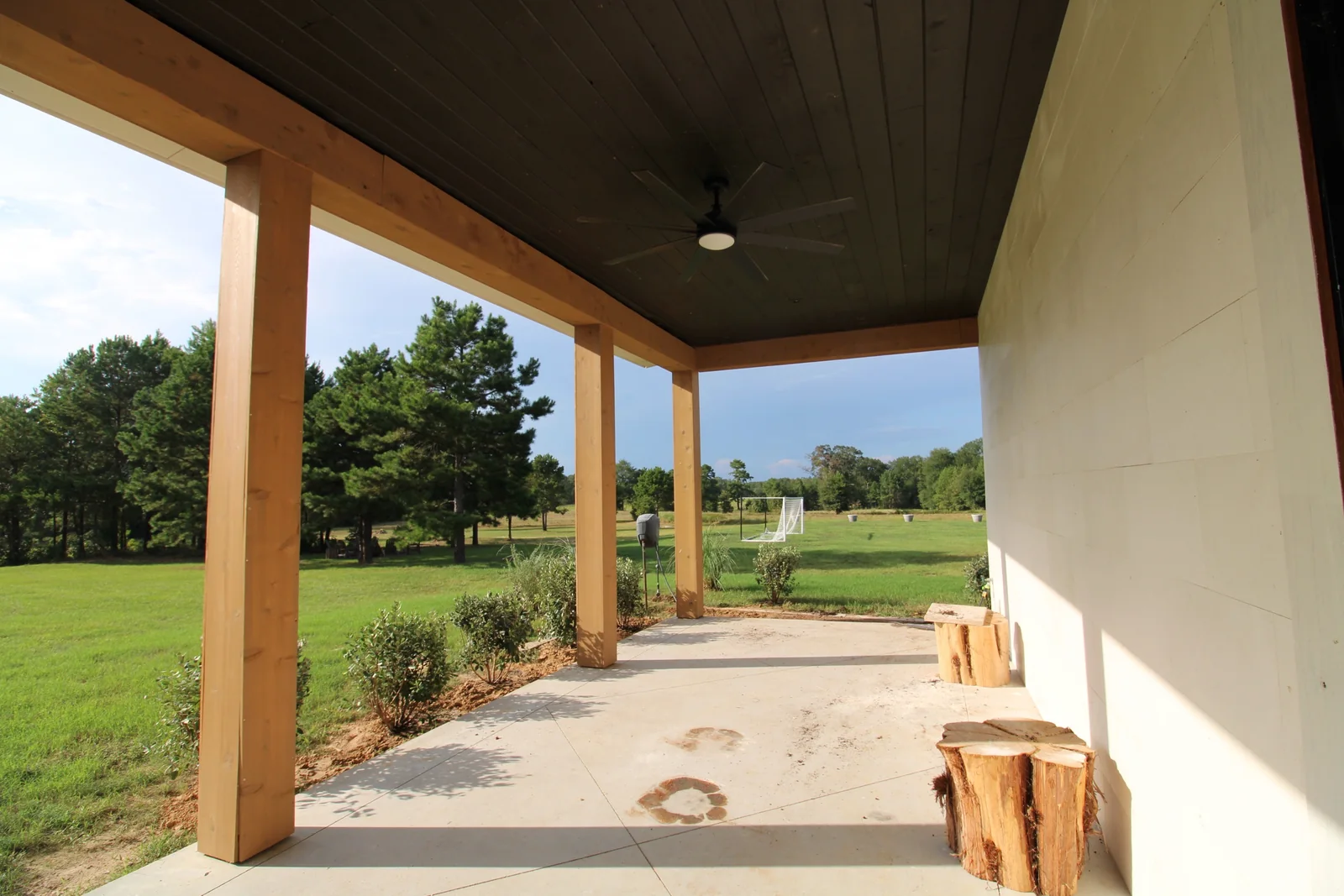 Covered porch with timber posts, ceiling fans, pale walls, and views across the lawn