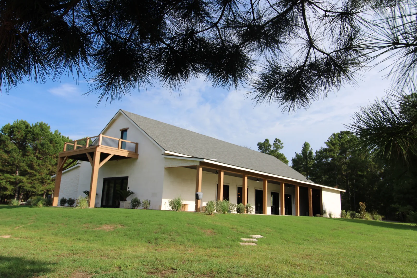 Ranch home with a long timber-columned porch and an upper deck, framed by pine branches